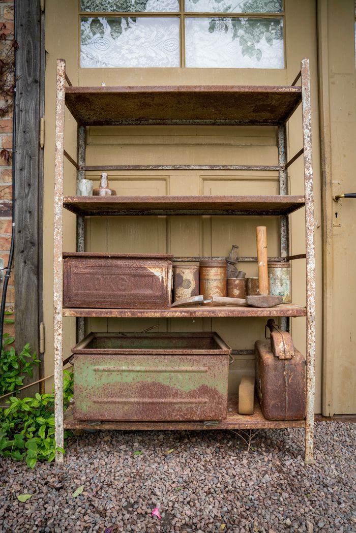 Weathered and rusty outdoor shelf with vintage containers and tools.